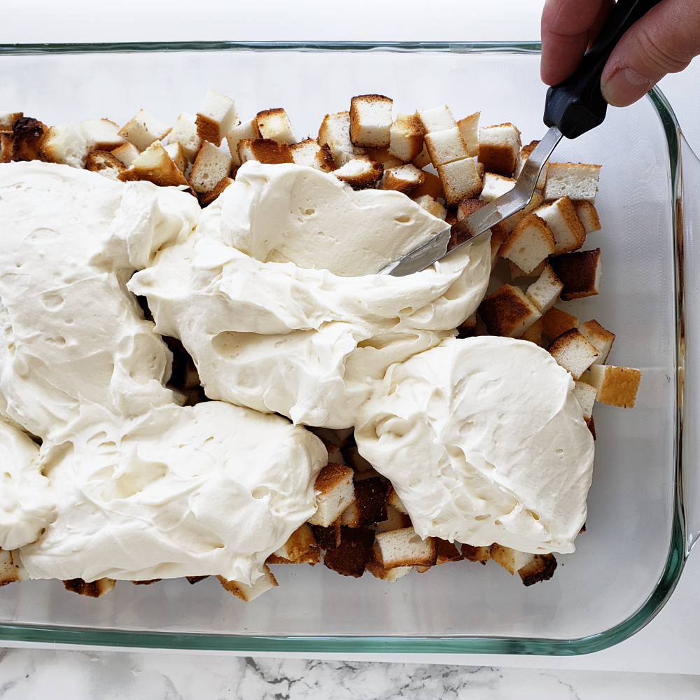 Spreading whipped cream layer over the diced cake cubes using an offset spatula 