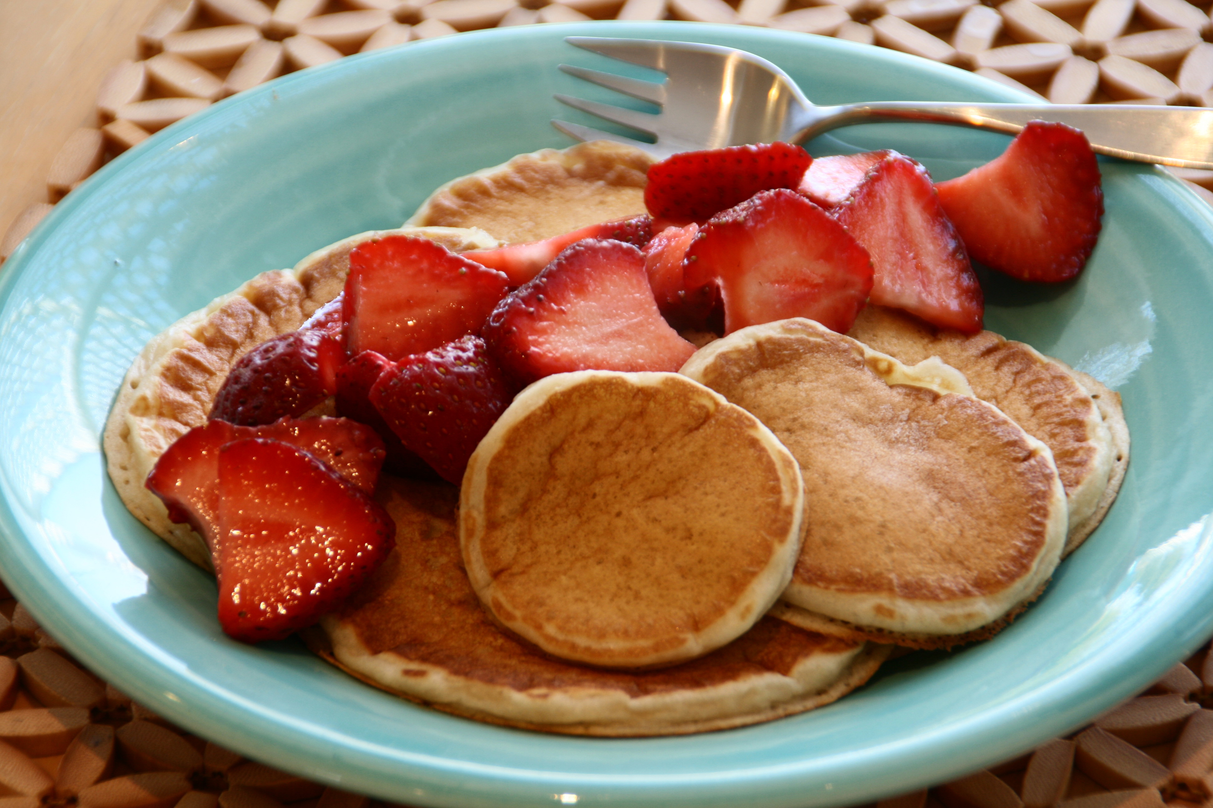 Pile of pancakes with strawberries on top on a turquoise plate with a fork resting at the top of the plate