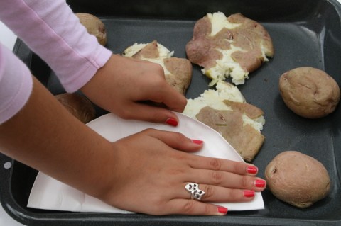 Hand pressing down on red potatoes to smash them. 