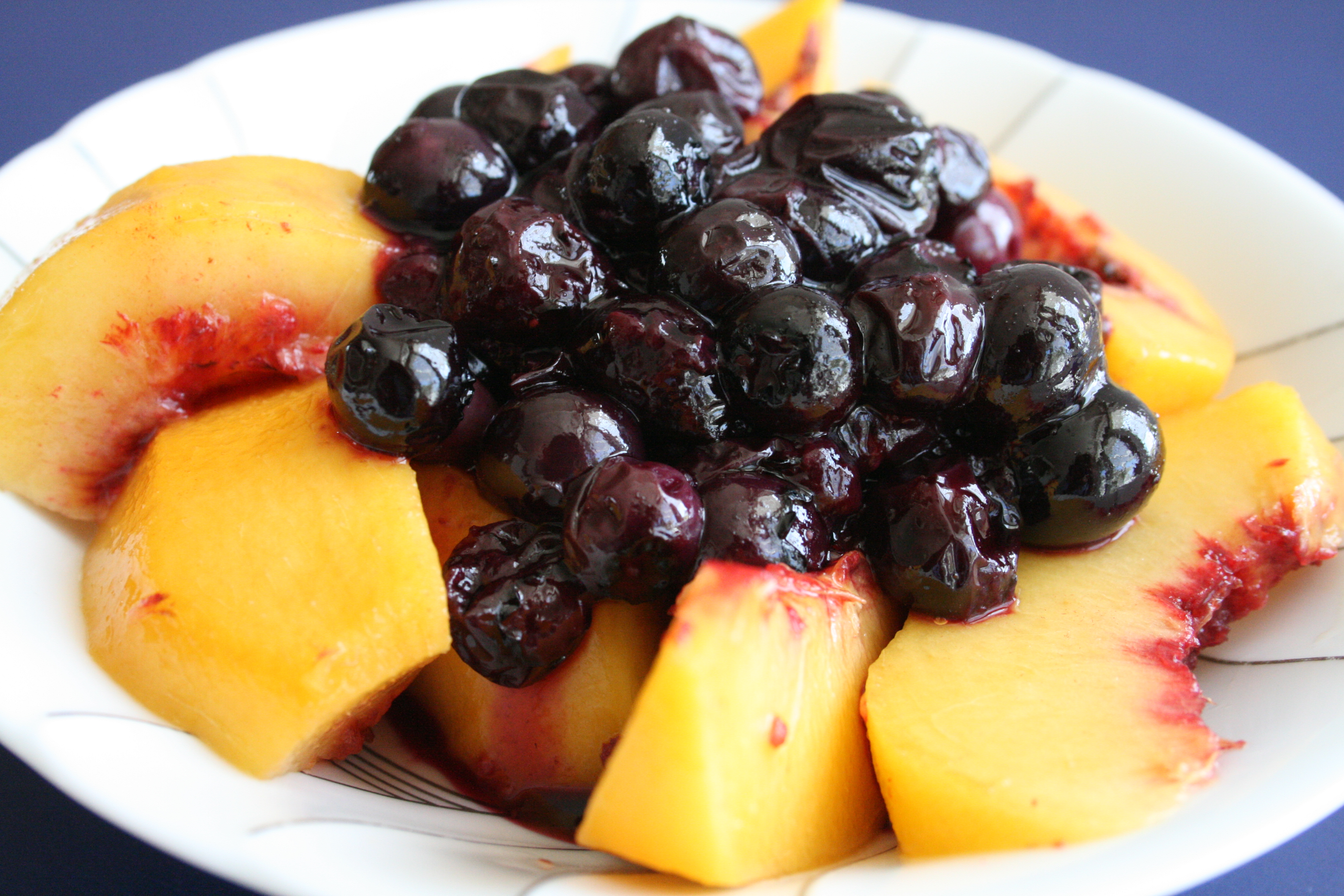 Blueberry Sauce on top of sliced peaches in a white bowl against a blue background