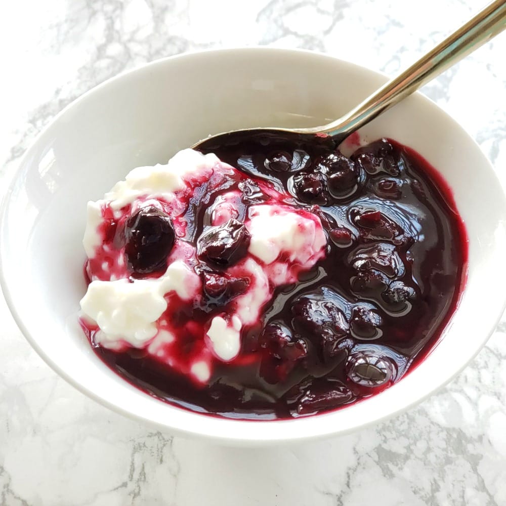 Blueberry sauce on cottage cheese in a white bowl with a spoon sticking out