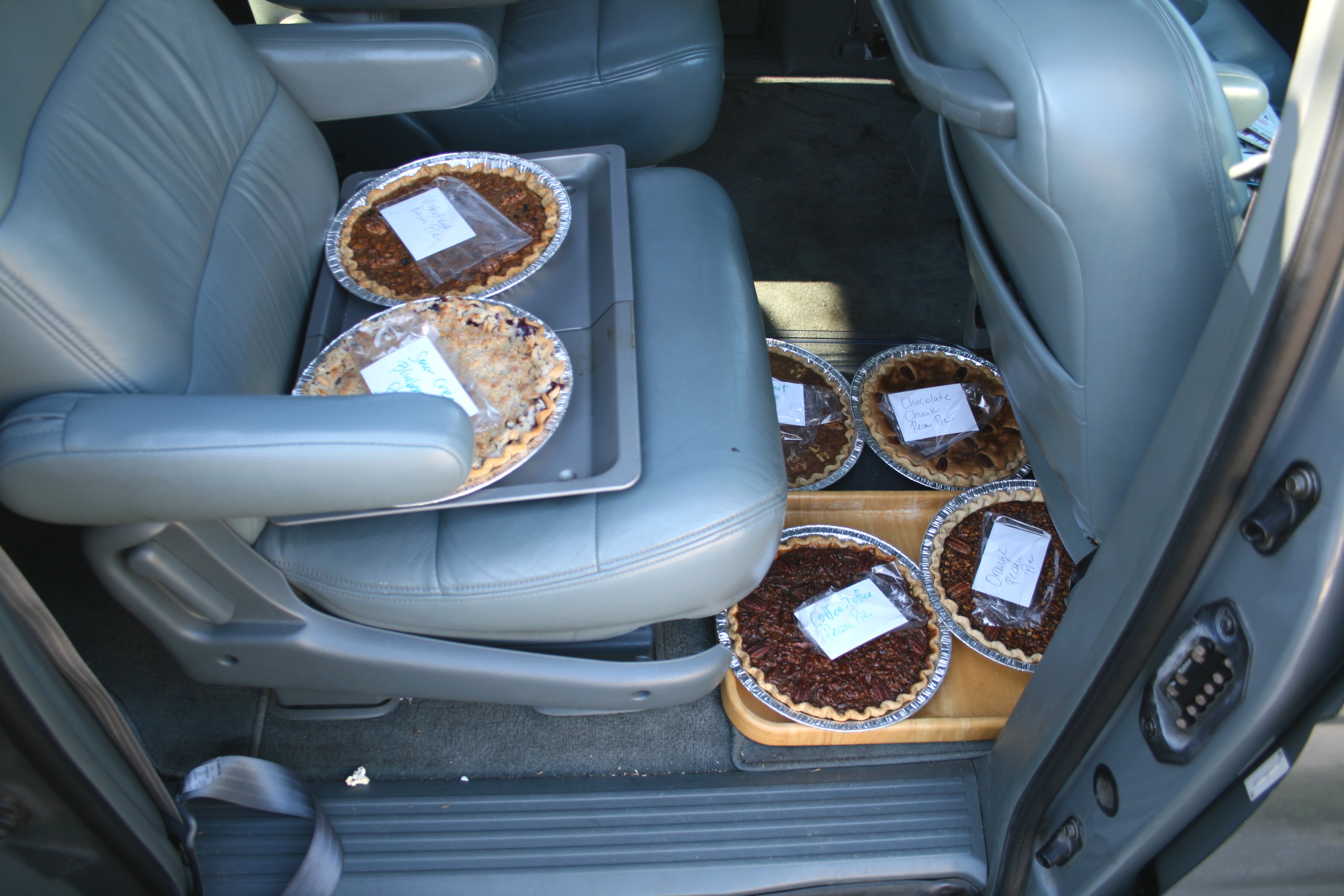 6 pies packed into the back seat of a grey mini van