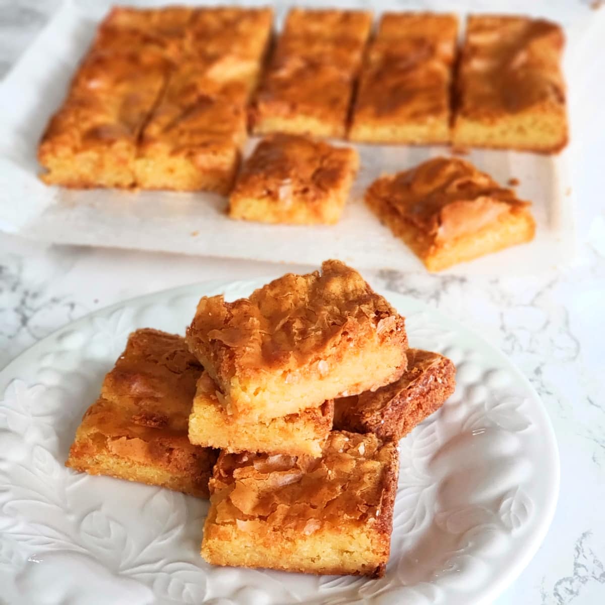 White Chocolate Blondies stacked on a white plate with the rest of the blondies in the background