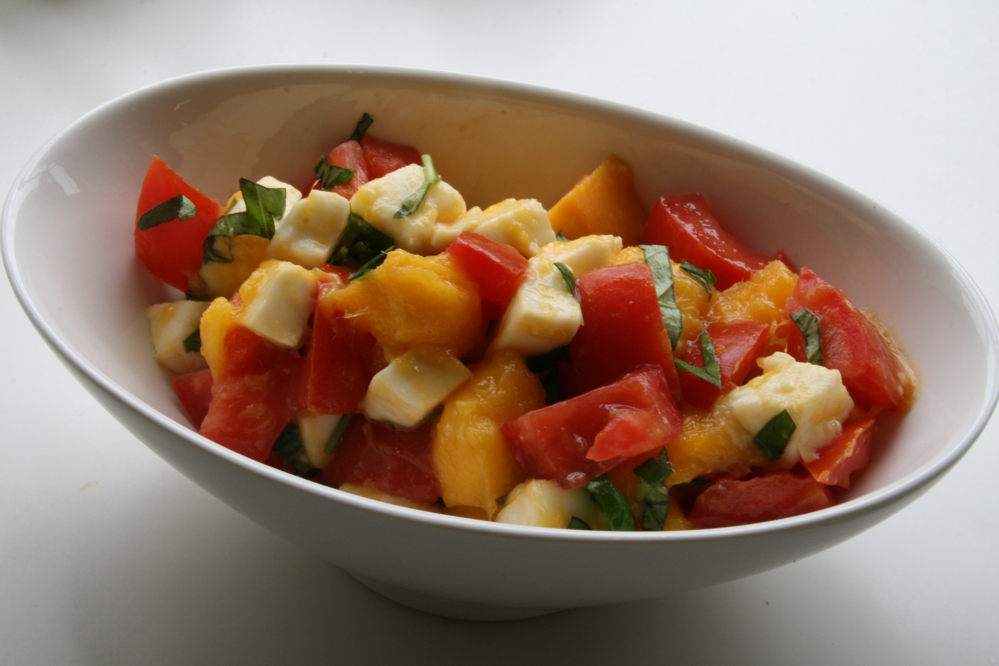 Diced mango, tomatoes and basil in an oblong white bowl