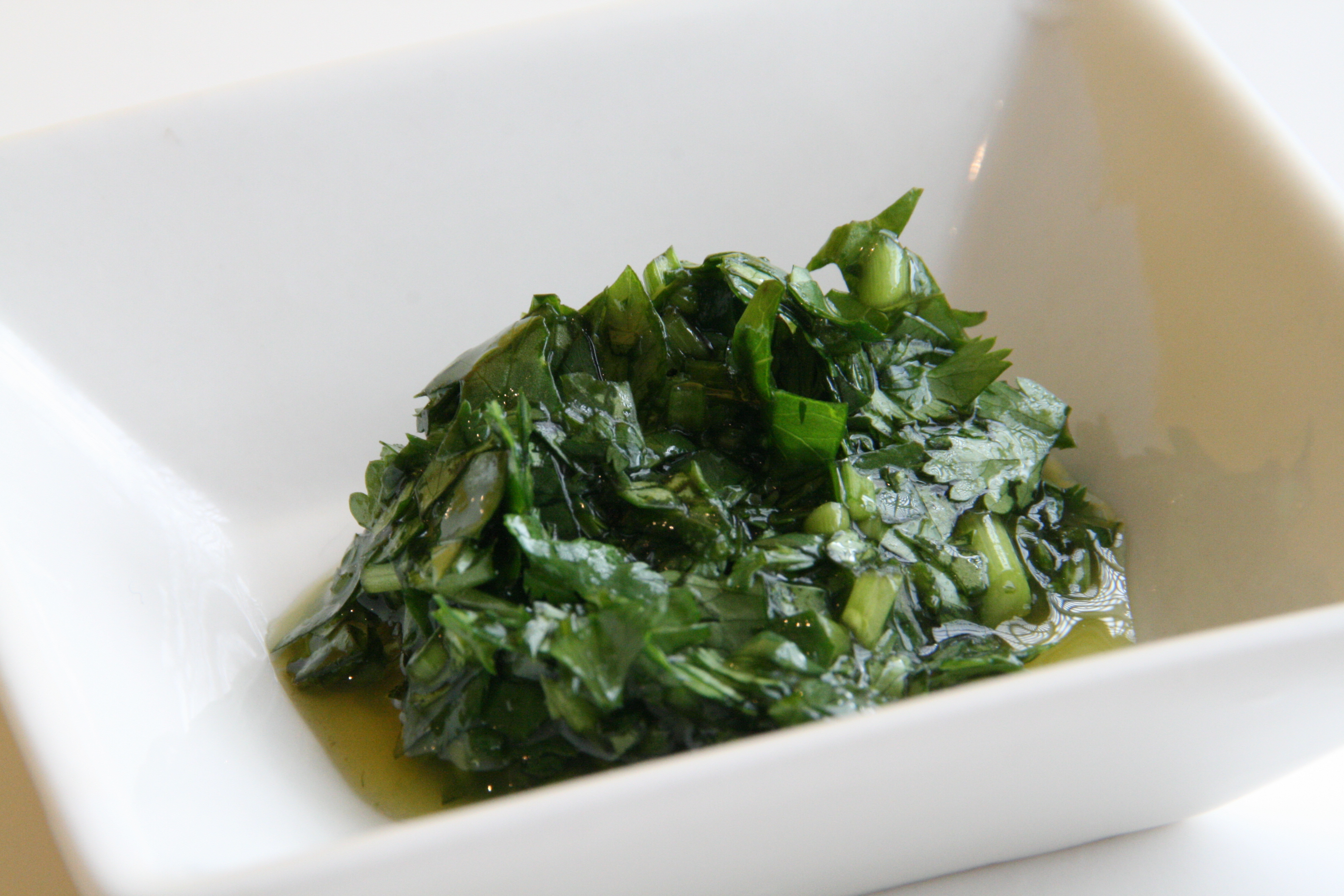Green chopped cilantro pesto in a white square bowl