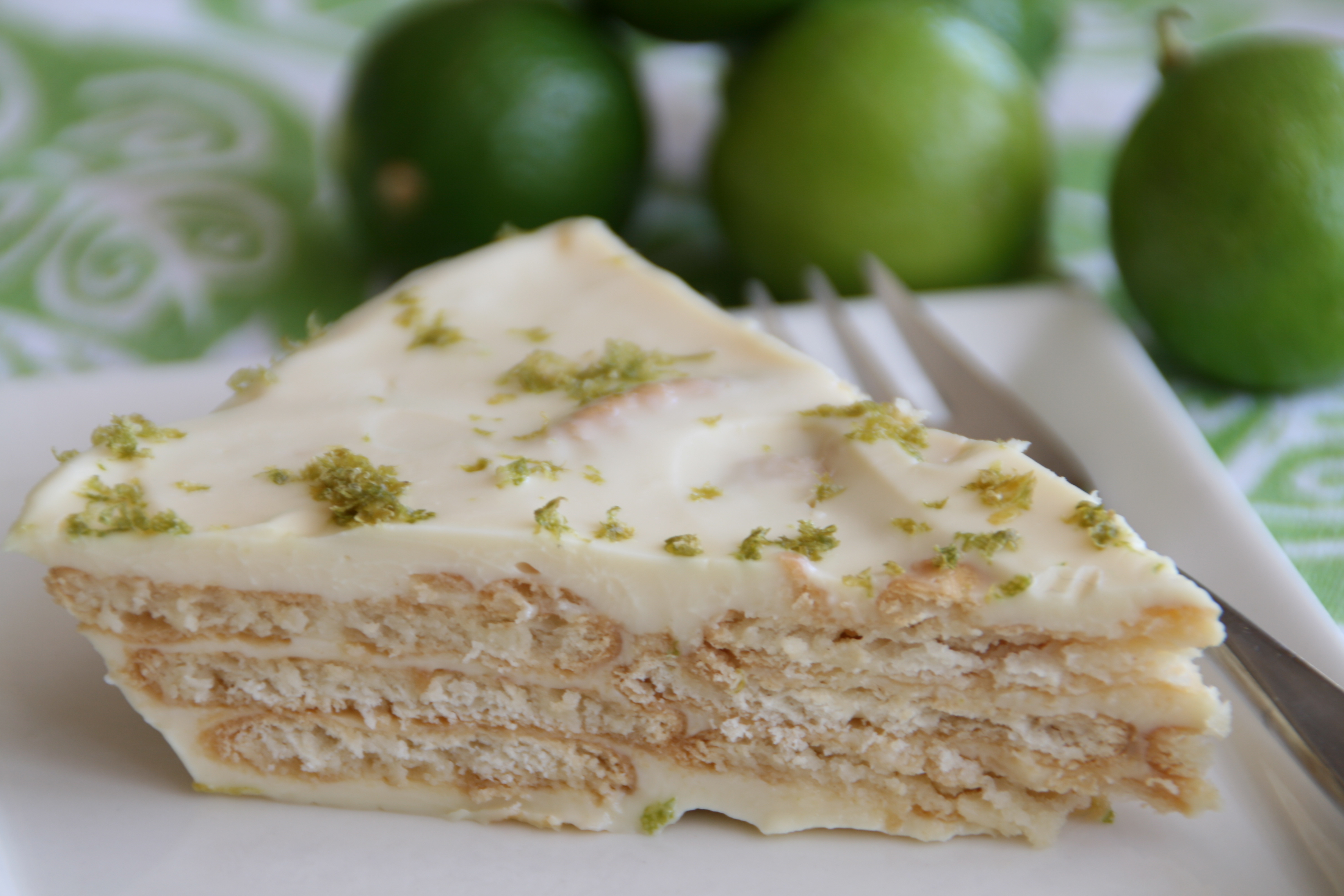 Slice of Key Lime Cracker Pie with green limes in the background