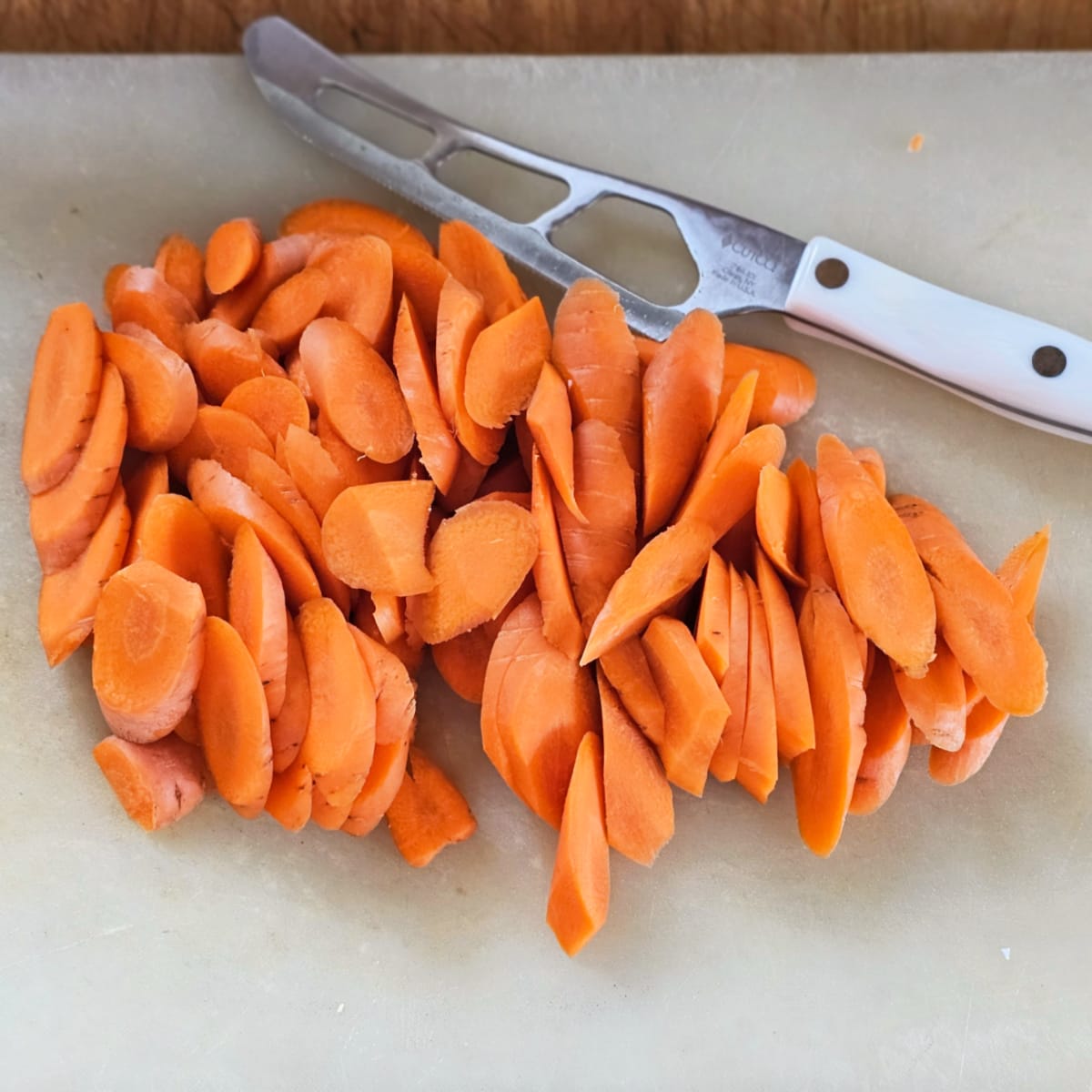 Cutting carrots on a cutting board with a white cheese knife