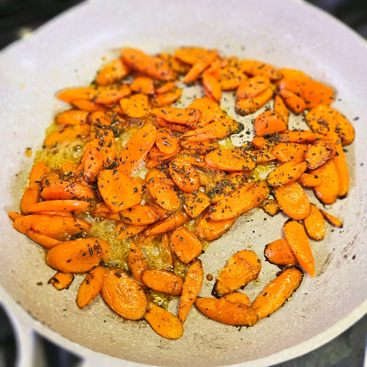 Honeyed Carrots with flecks of minced rosemary on top in a light colored skillet