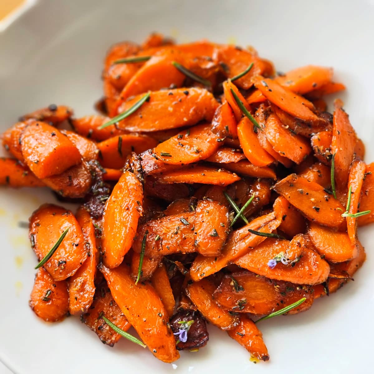 Bright orange cooked carrots flecked with rosemary in a white bowl.
