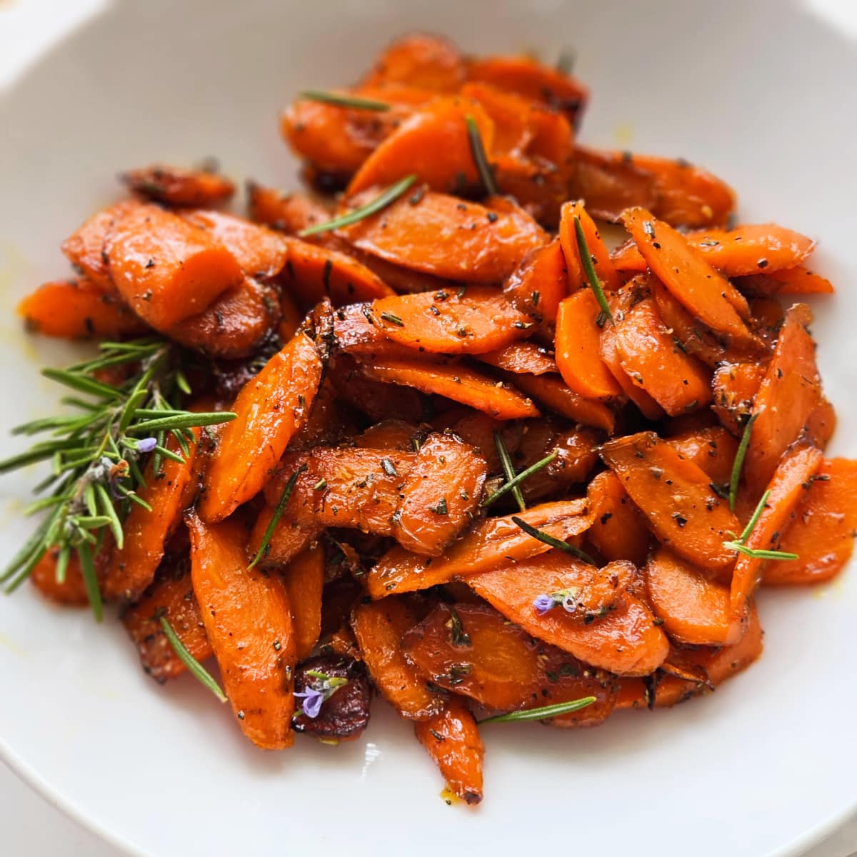Honeyed Carrots with green rosemary flecks and a sprig of rosemary on the left side