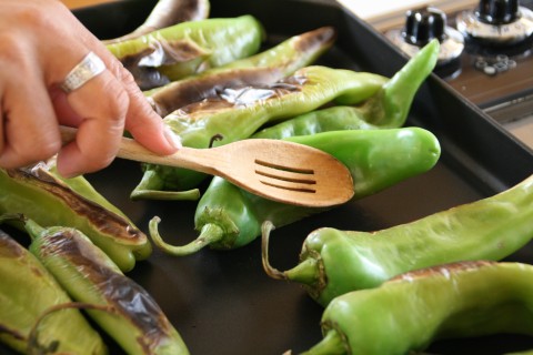 Wooden spoon tamps down Hatch chile on griddle