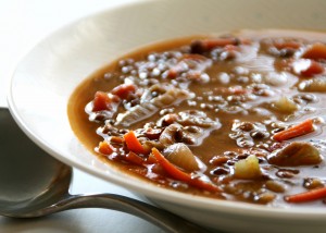 White bowl of brown-ish lentil soup with vegetables sticking out of the top