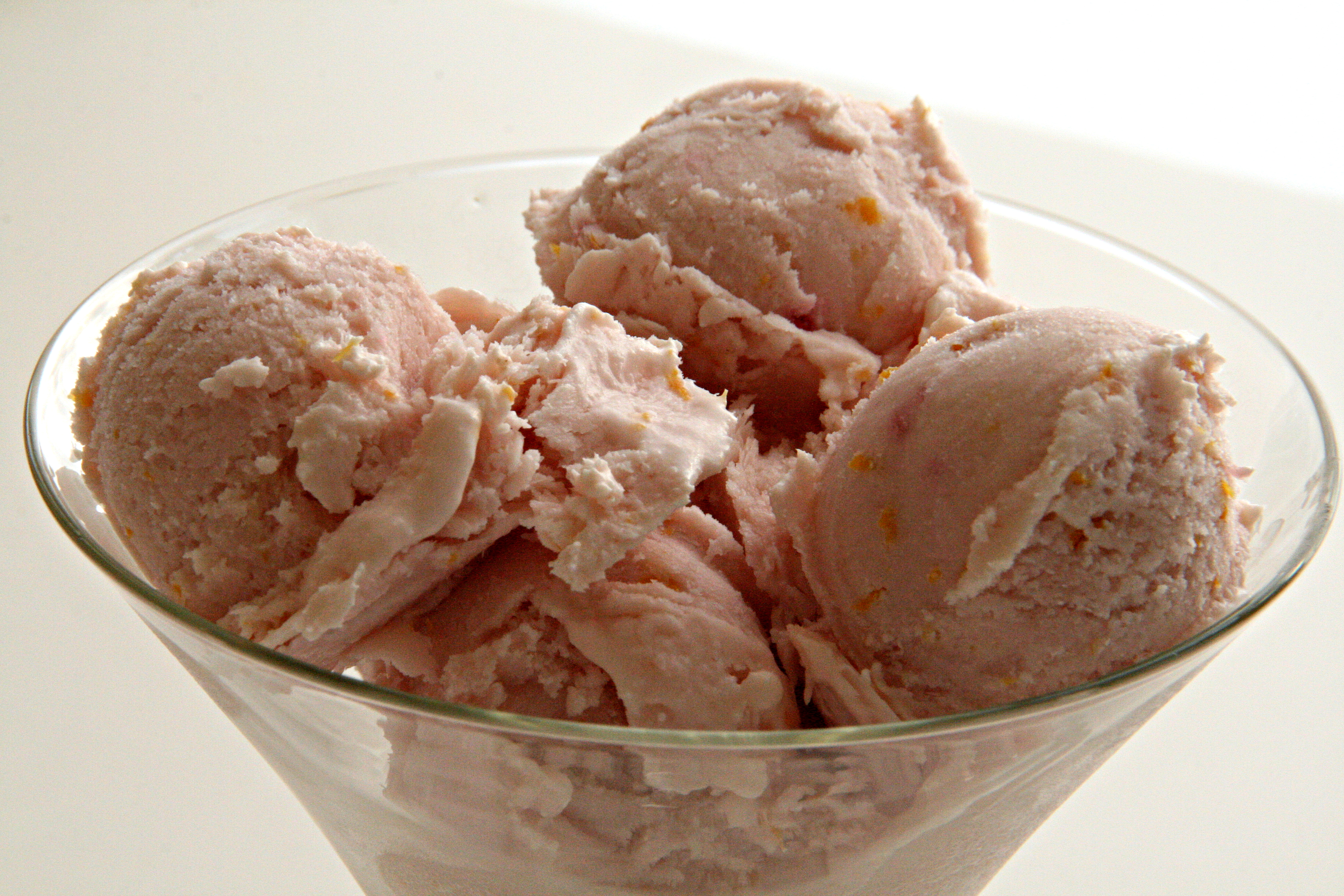 Small scoops of light pink blood orange ice cream in a clear glass bowl