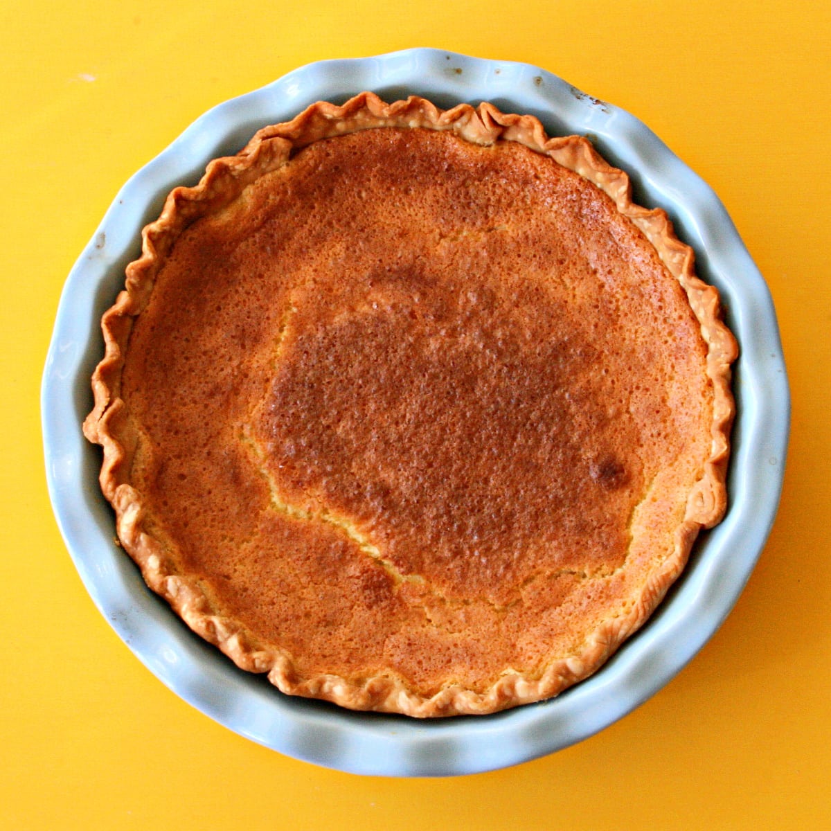 Meyer Lemon Chess Pie in a blue pie dish against a yellow background