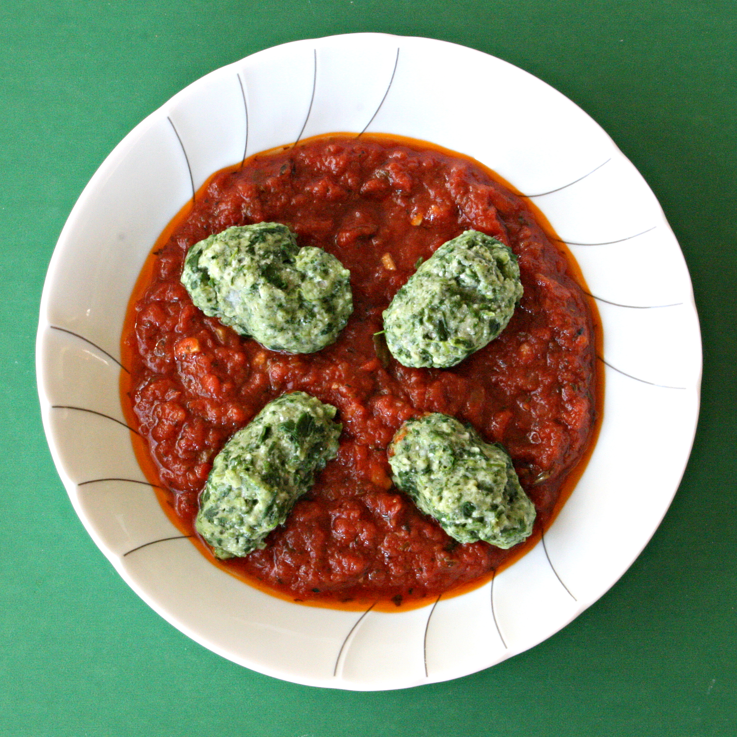 Gnudi Ravioli in red sauce in a white bowl against a green background