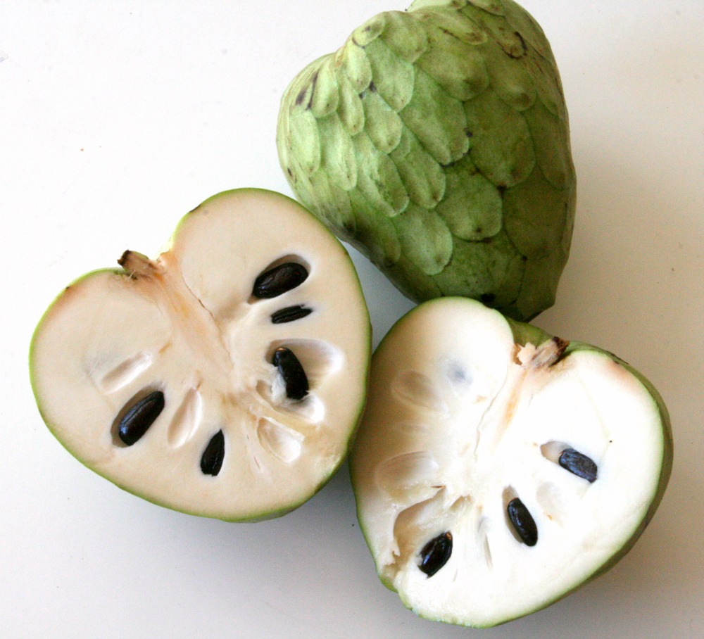 cherimoya cut open in foreground, whole green cherimoya in background