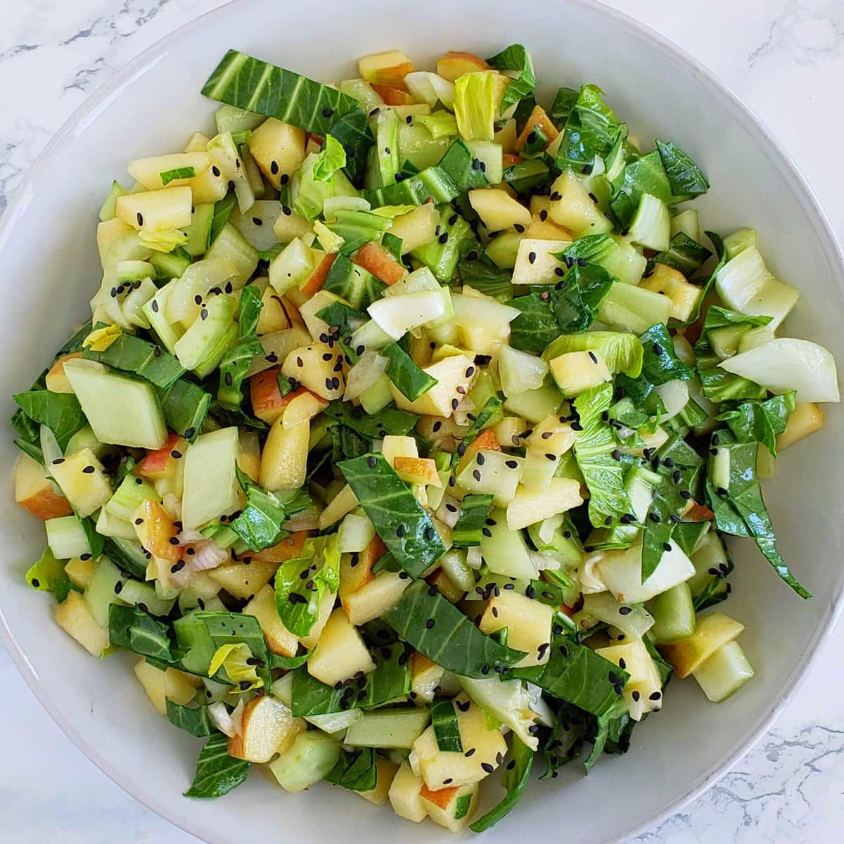 Chopped salad speckled with black sesame seeds piled into a white bowl sitting on a marble counterlad easy recipe on ShockinglyDelicious.com