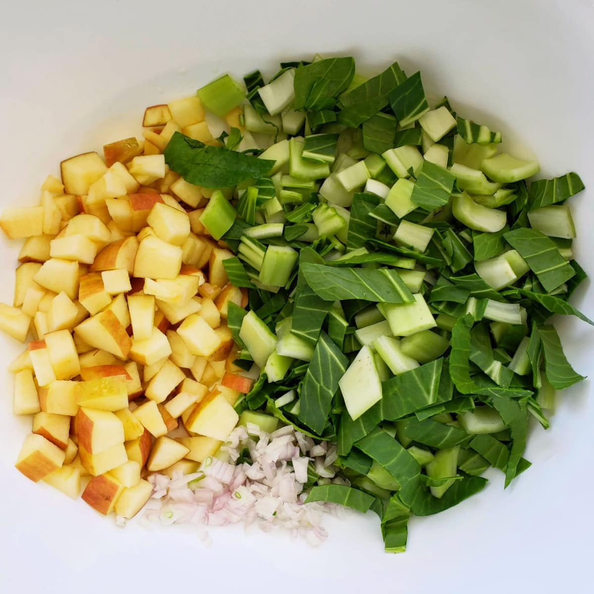 Aerial view of chopped baby bok choy, apple and shallot in a white mixing bowl