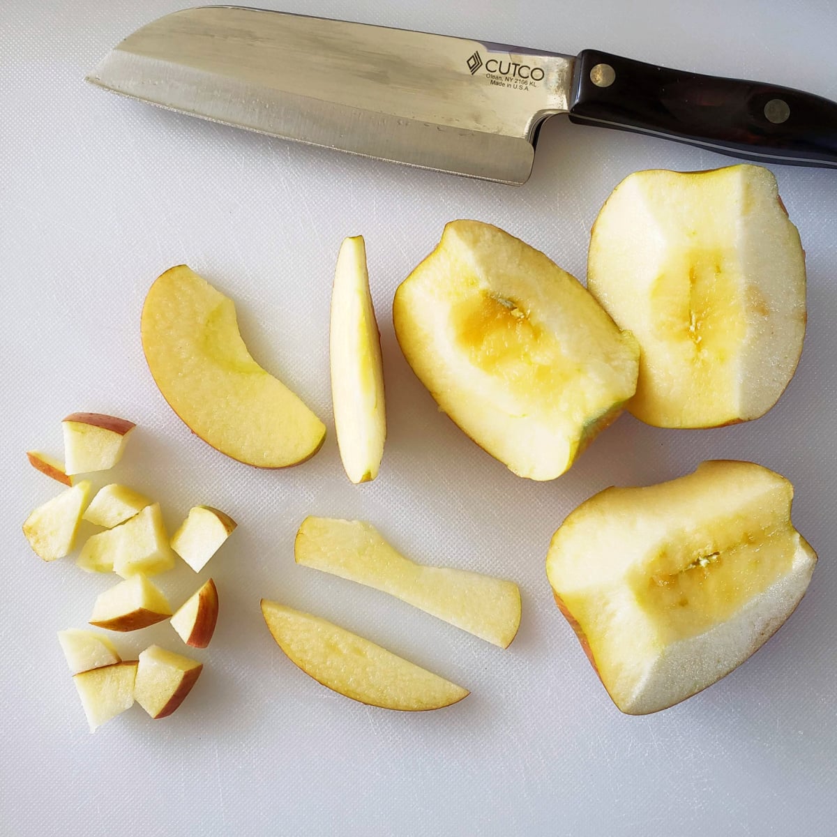 Chopping an apple in a small dice on a white cutting board, with a chef's knife alongside