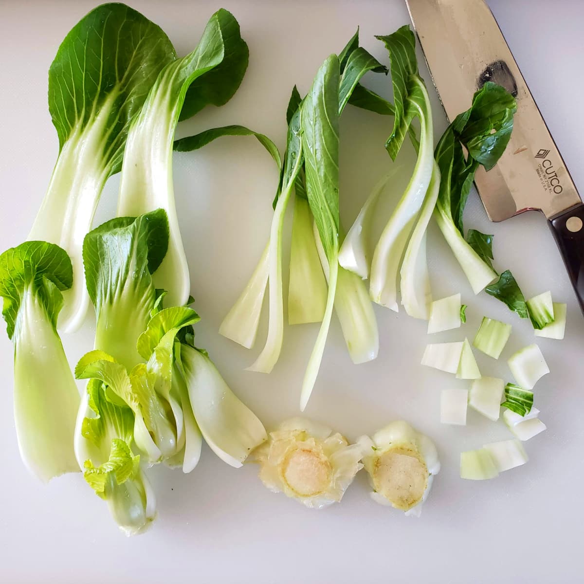 Cutting baby bok choy on a white cutting board with a chef's knife alongside