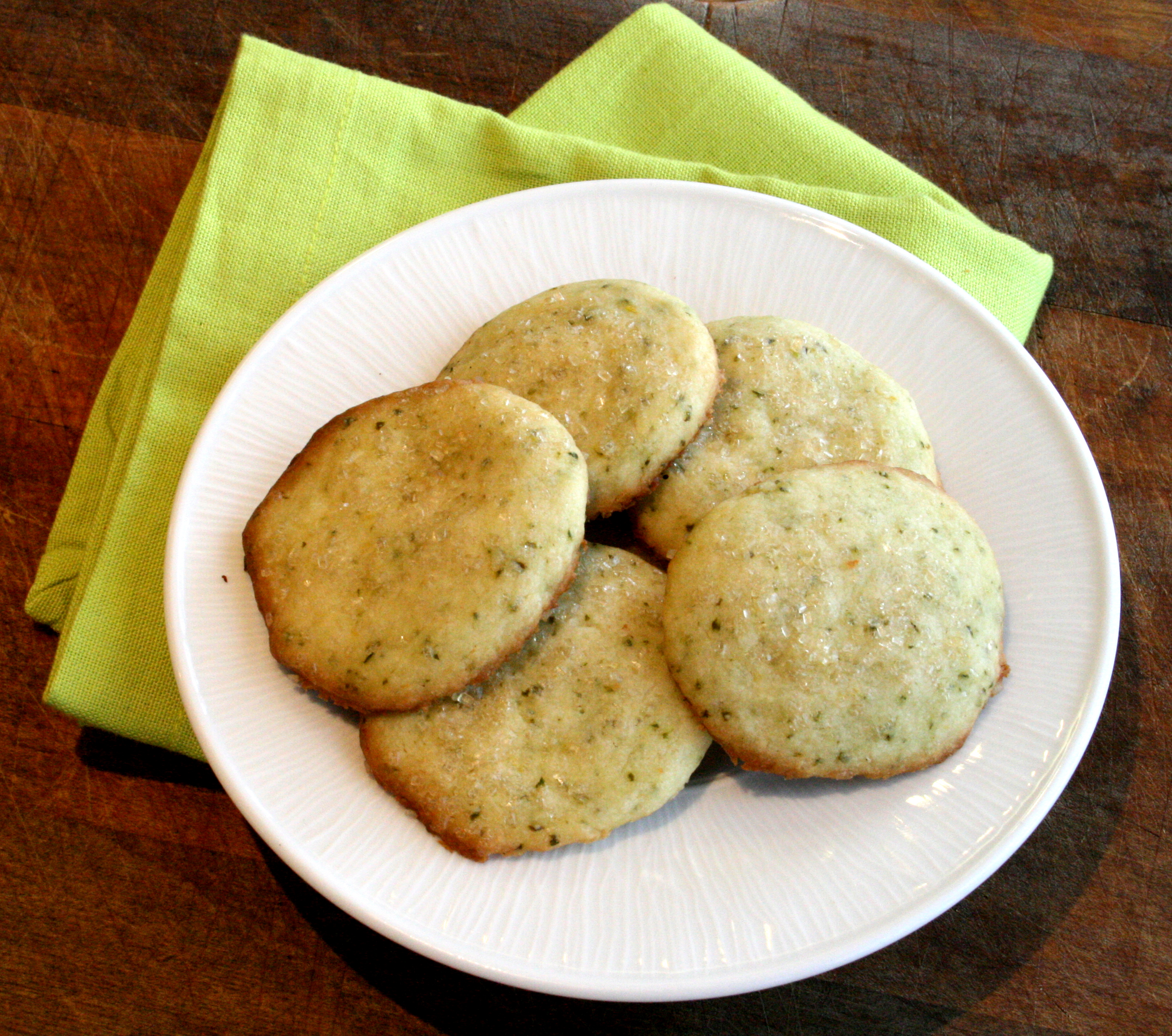 5 Lemon-Lime Basil Shortbread Cookies on a white plate sitting on a bright green cloth napkin