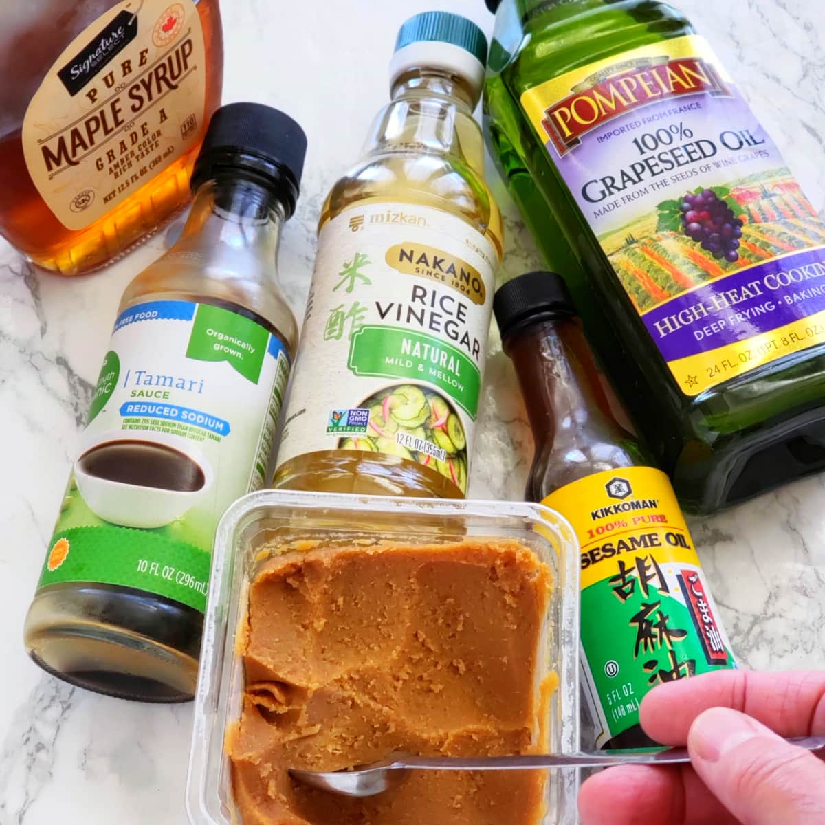 Ingredients for Sweet Miso Dressing -- maple syrup, tamari, rice vinegar, grapeseed oil, white miso and sesame oil on a marble countertop