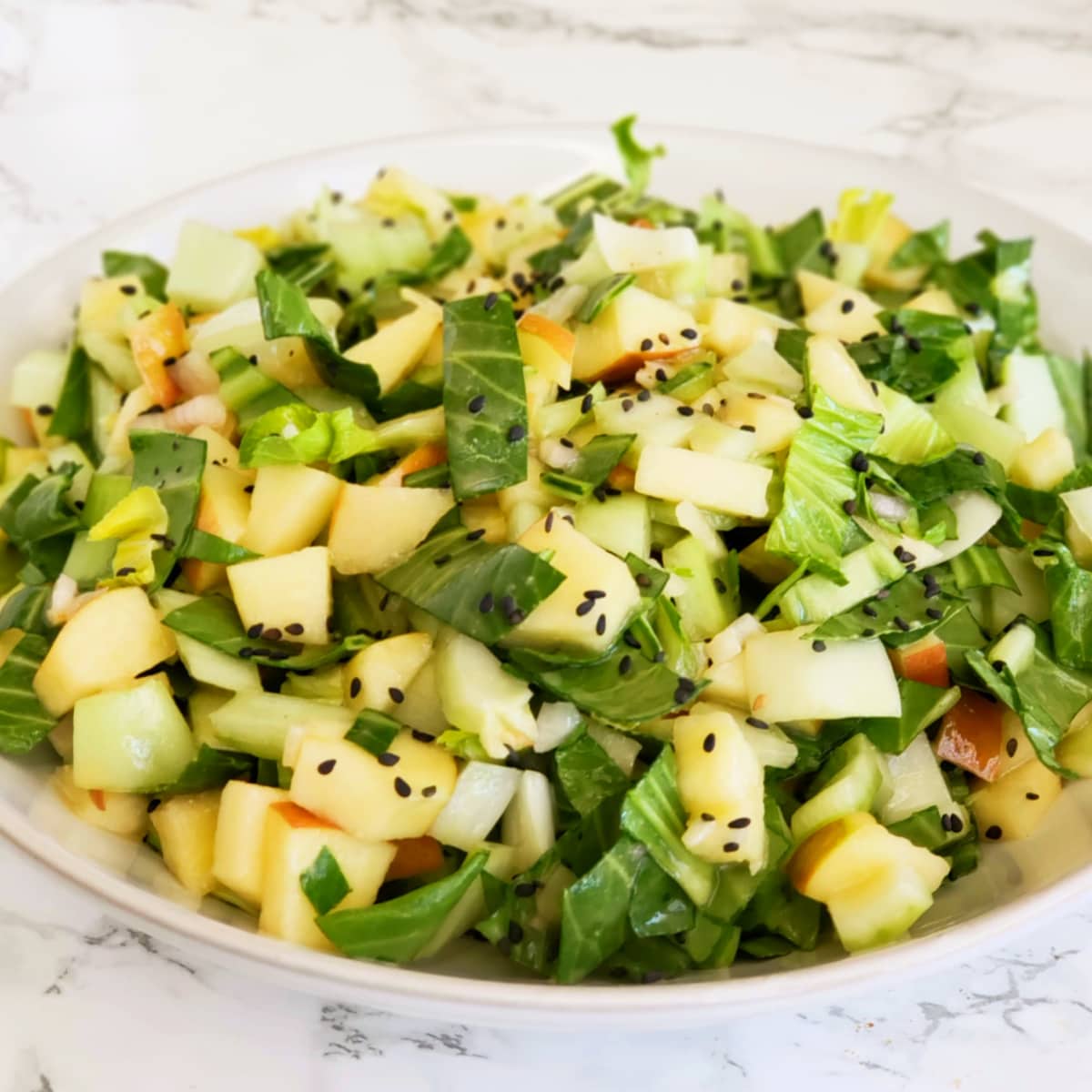 Lemony Baby Bok Choy, Apple and Miso Salad in a white bowl on a white marble counter top