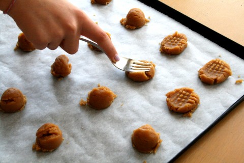 Woman's hand pressing fork tines into the top of peanut butter cookies