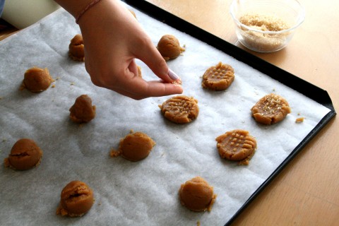 Hand sprinkling sugar on top of peanut butter cookies