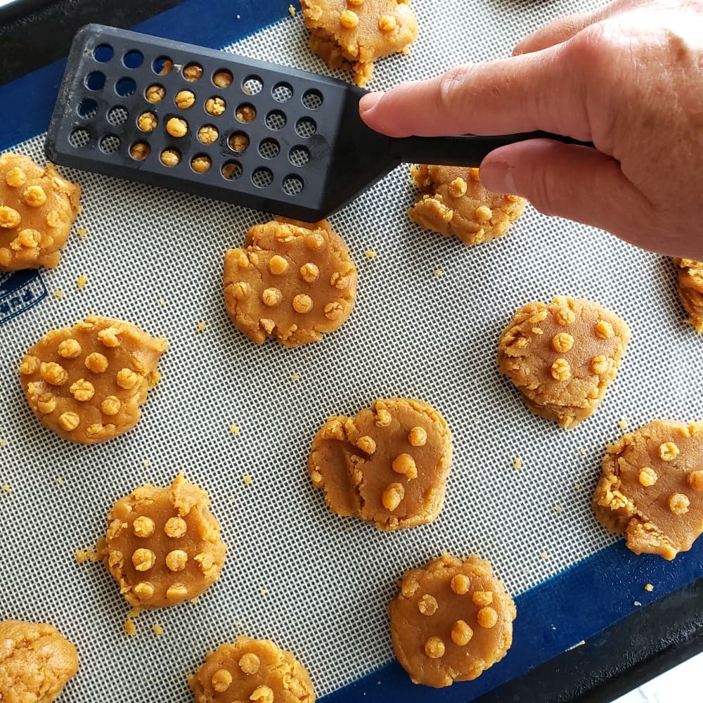 Black spatula pressing down on cookies to make a pattern