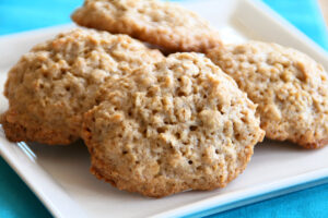 4 brown cookies stacked on a white square plate set on a bright blue cloth