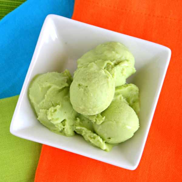 Small scoops of Avocado Lemon Grass Ice Cream in a square white bowl against an orange, green and blue background