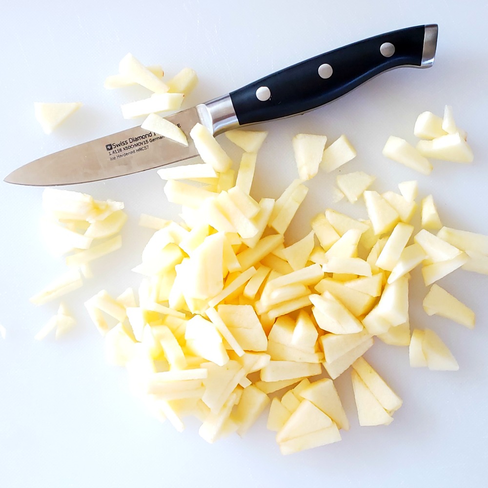 Finely chopped apples on a white board with a black-handled knife