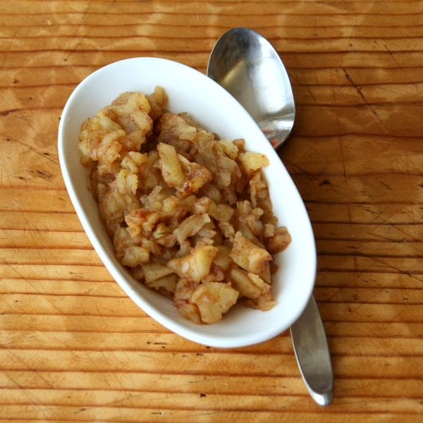 Applesauce in a white bowl on a wooden cutting board with a spoon alongside