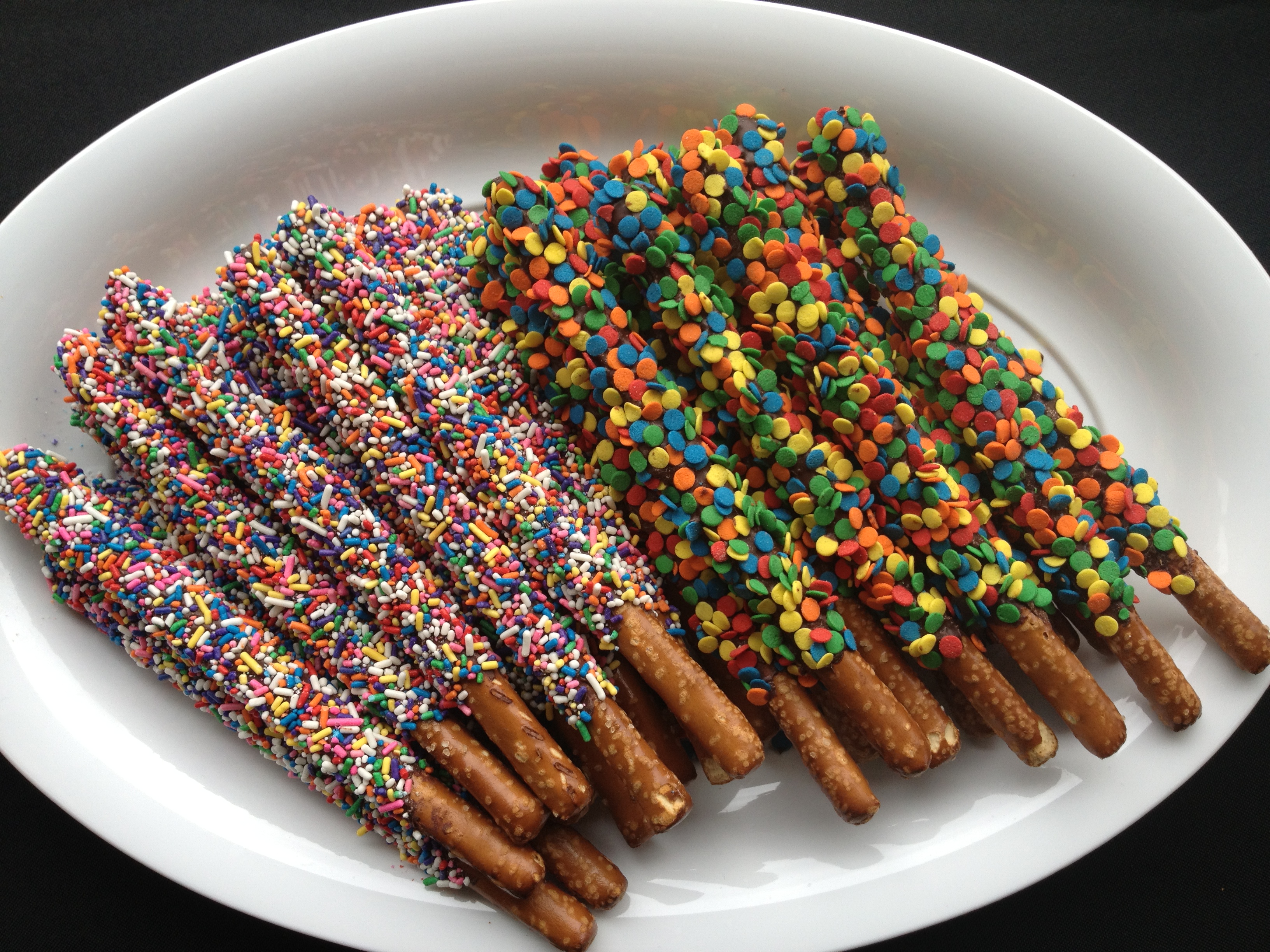 Festive Pretzel Rods lined up on a white plate for a bake sale. 