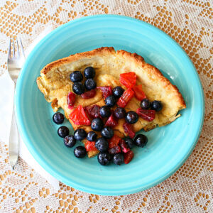 Dutch Baby Pancake on a turquoise plate with a fork to the left side of the plate on a lace tablecloth