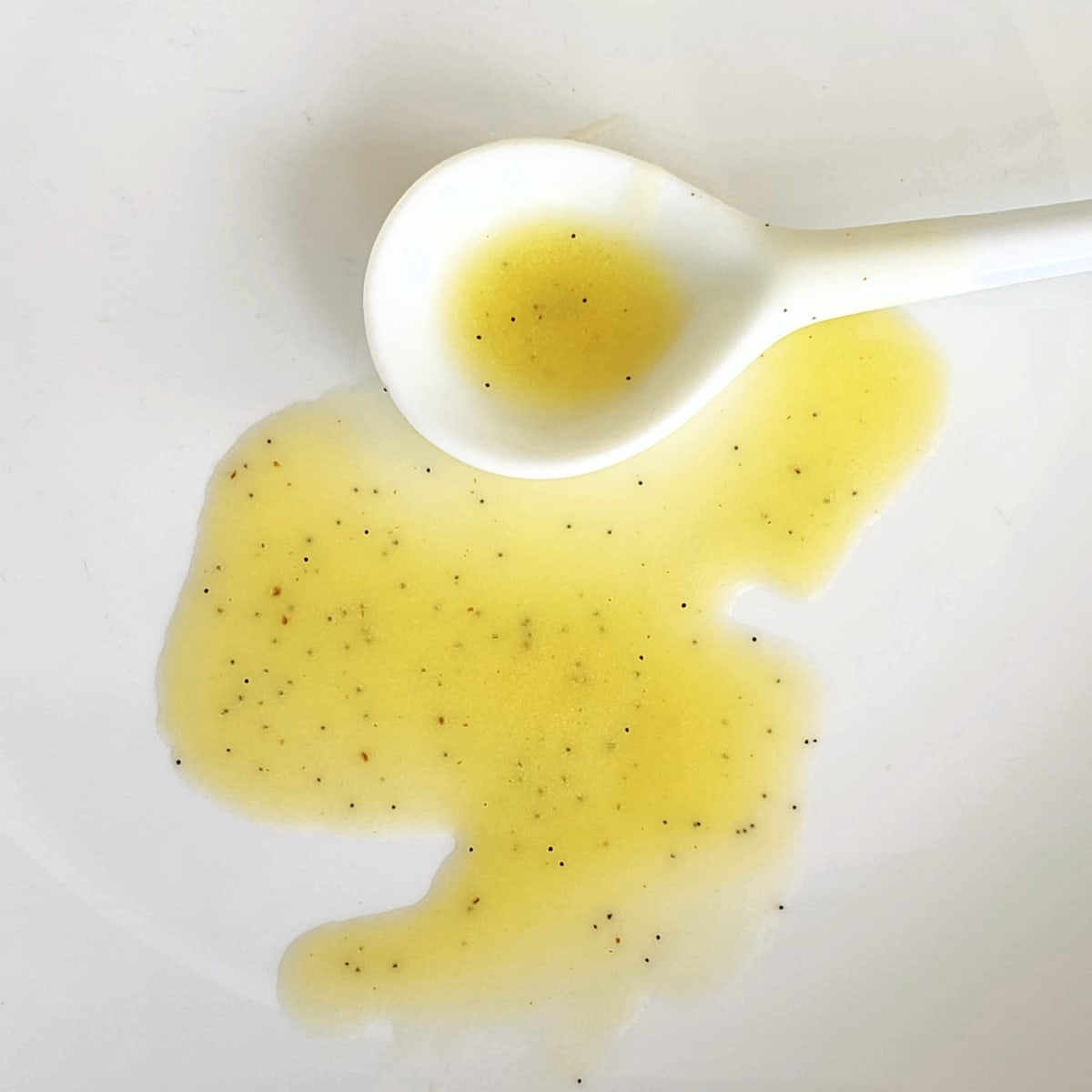 Easy Meyer Lemon Vanilla Salad Dressing spilled on a white plate with a white ceramic spoon alongside itDelicious.com