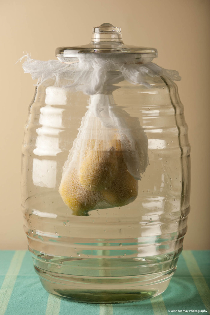 Large jar with whole lemons hanging in a cheesecloth bag inside it, to make limoncello. 