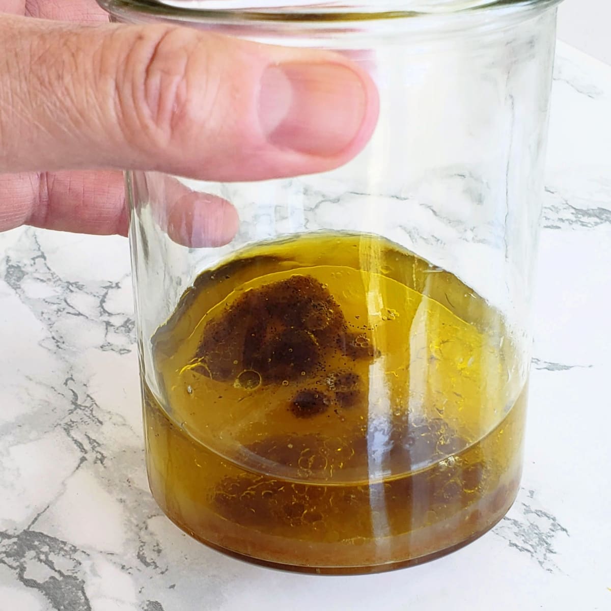 Hand holding a jar with salad dressing ingredients in it, ready be blended, with a white marble counter in the background