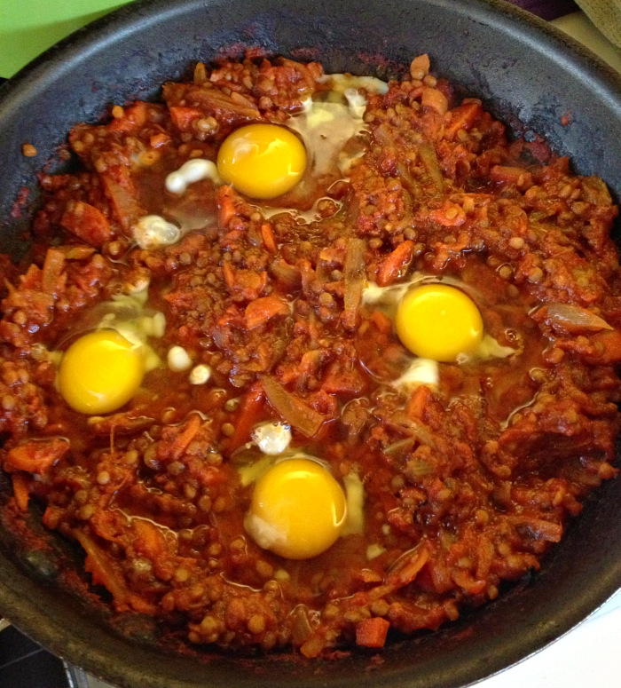 4 eggs atop a reddish bed of tomatoes and lentils in a black skillet 