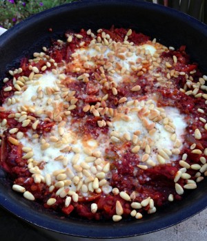 4 cooked eggs with pine nuts sprinkled on top, resting on reddish lentils in a black skillet