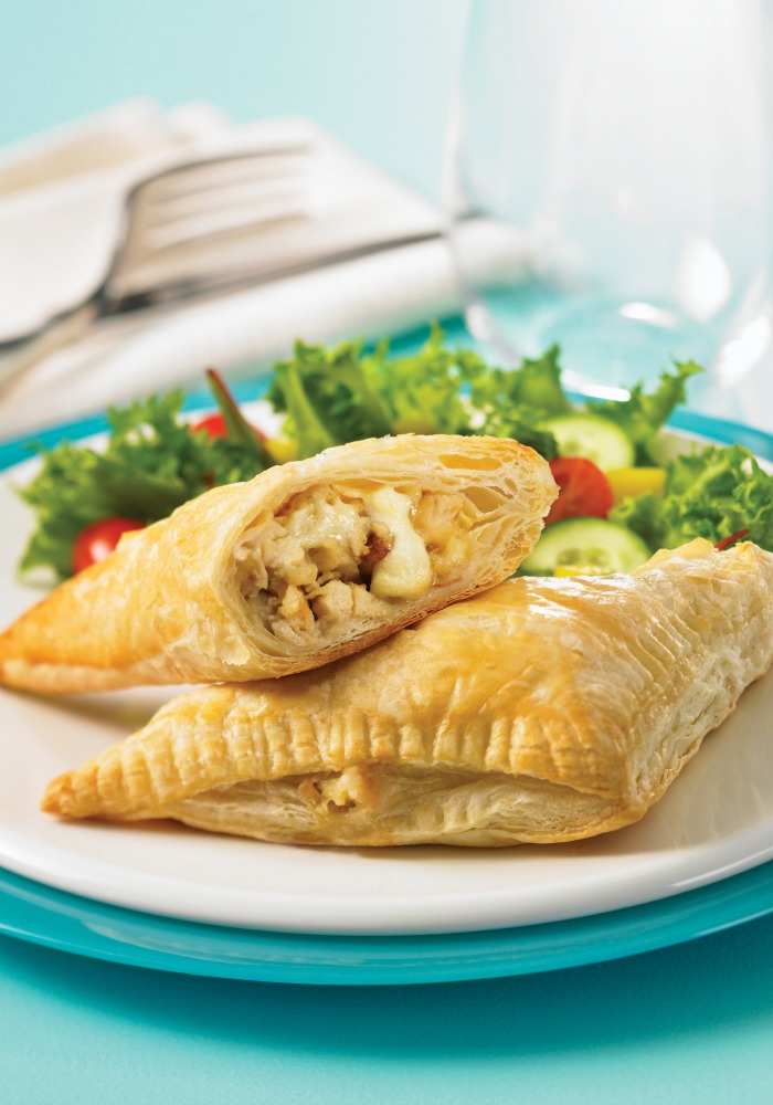 2 puff pastry turnovers on a white plate with a salad in the background
