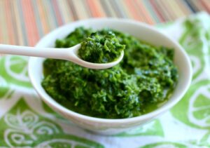 White bowl of green pesto-like sauce, with a white spoon above the bowl.