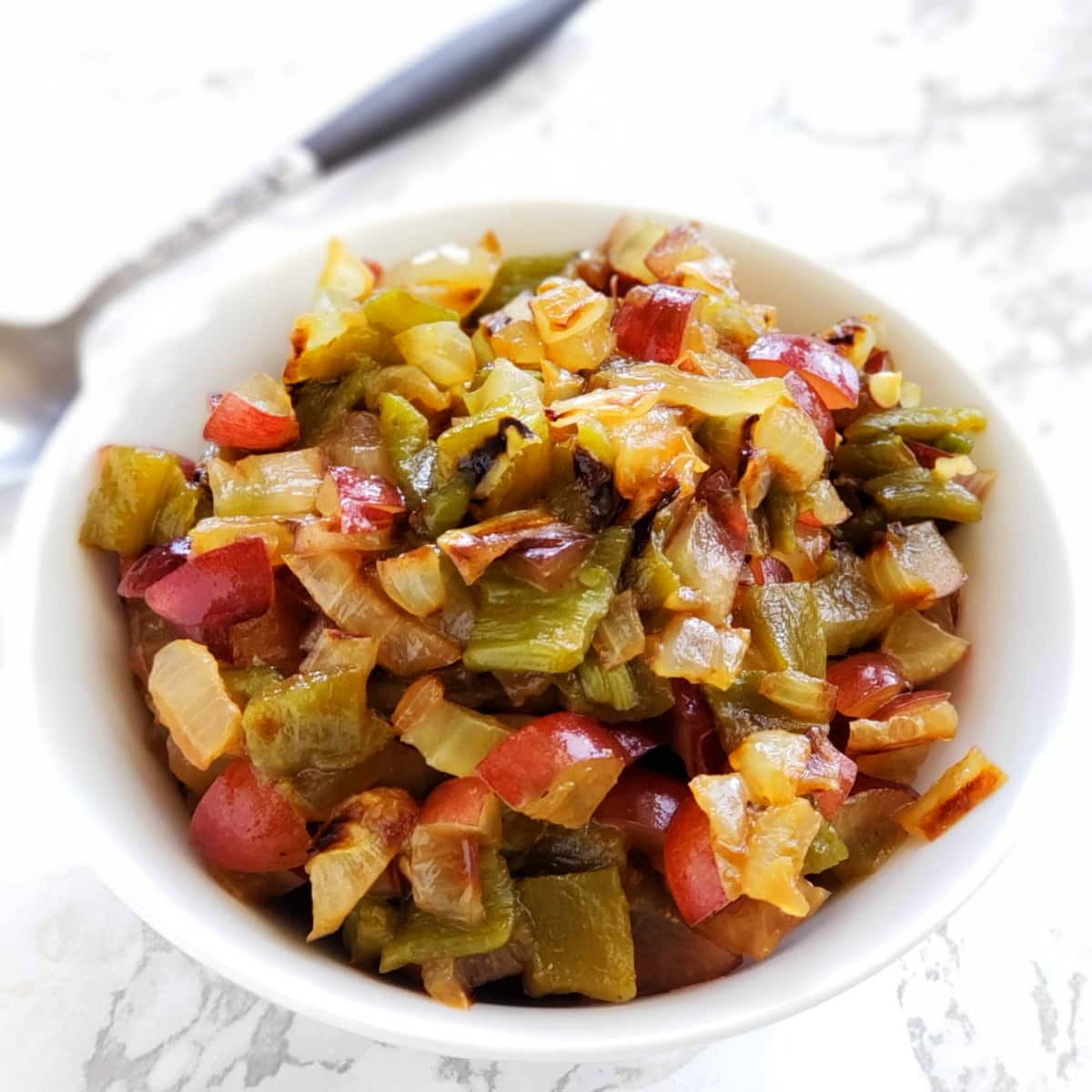 Hatch Chile, Grape and Grilled Onion Salsa in a white bowl on a white marble counter with a serving spoon in the background on Shockingly Delicious