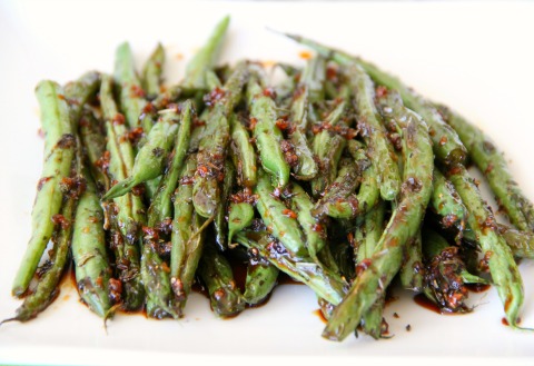 Green beans on a white plate with crisped flecks on top