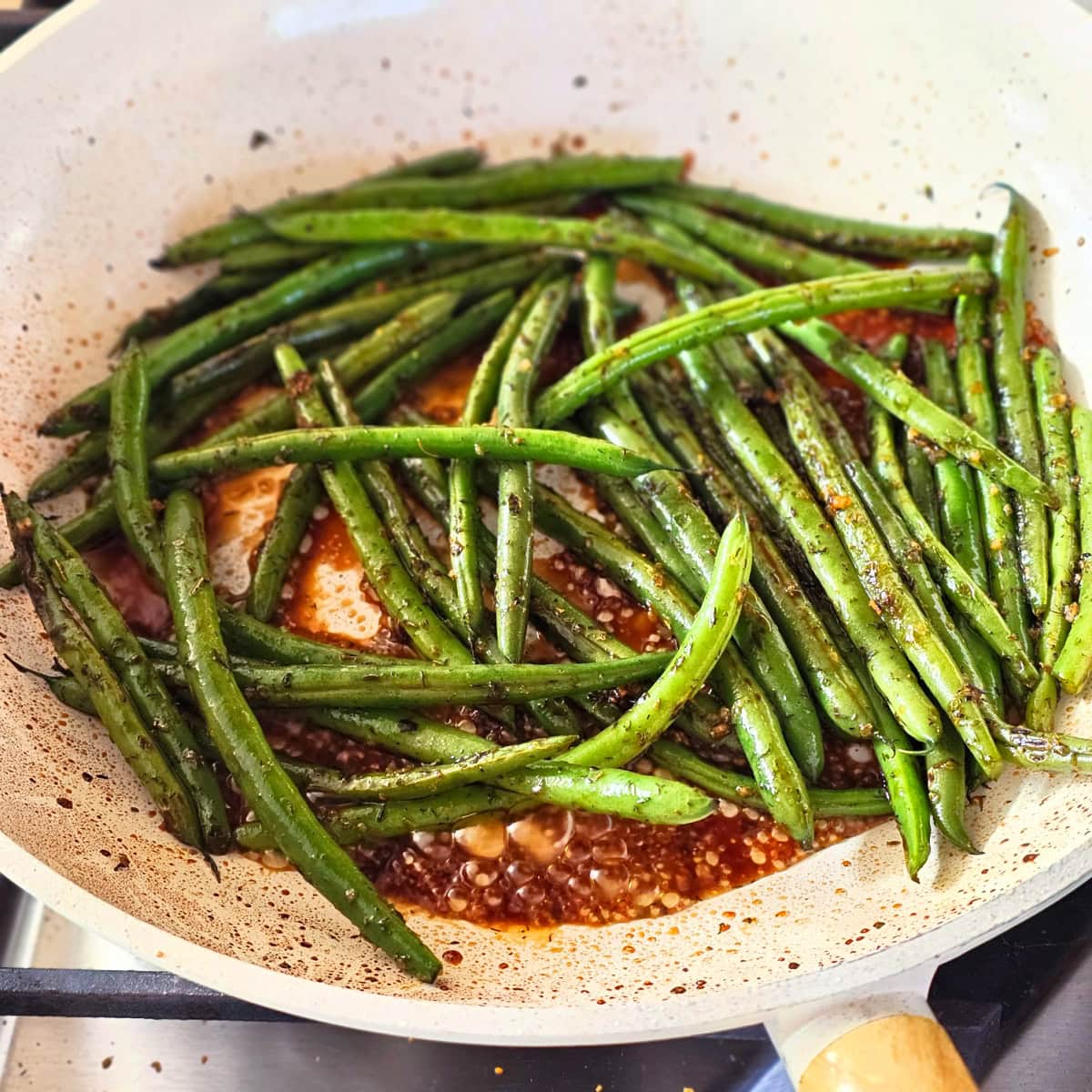 Soy sauce agave and water with green beans in the cream-colored skillet for Sweet and Savory Green Beans