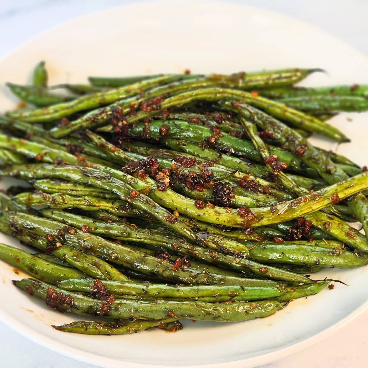 Sweet and Savory Green Beans with brown garlic and herbs on top in a white bowl 
