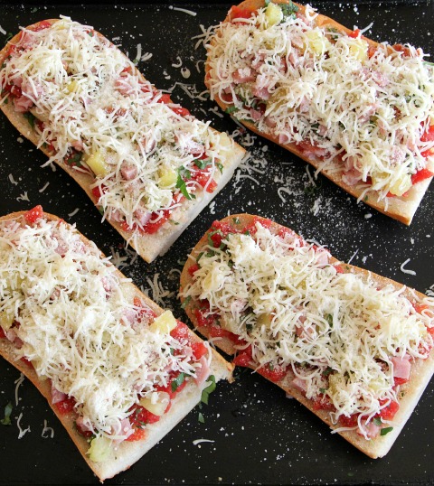 4 French bread pizzas ready for the oven with grated Parmesan on top