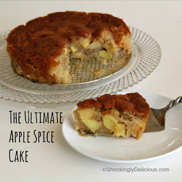 Apple cake on a pedestal plate with a piece remove and displayed on a white plate in the foreground