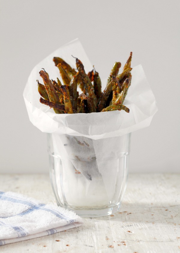 Green Bean Fries in waxed paper in a glass, sitting on a counter top with a tea towel alongside